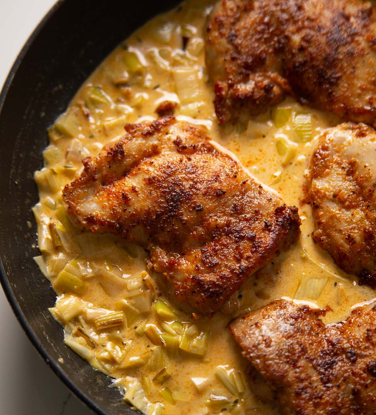 close up shot of chicken thigh in large pan with creamy leeks