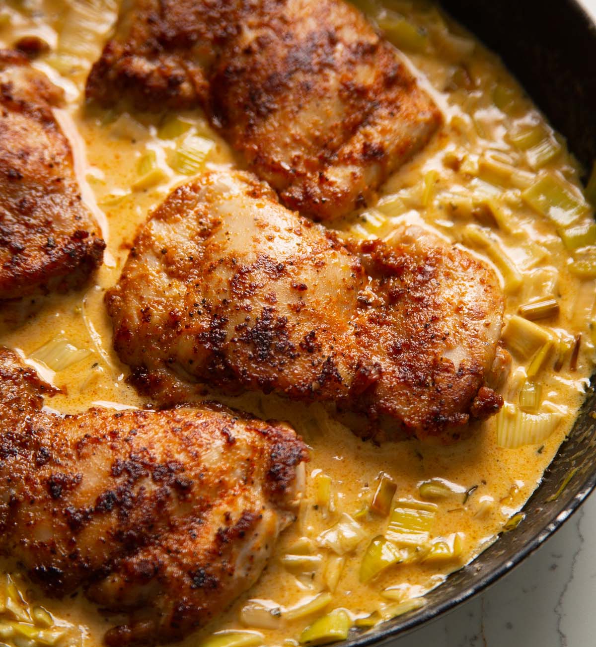 close up shot of chicken thighs on bed of creamy leeks in large pan