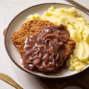 sausage schnitzel on white plate with onion gravy and mash