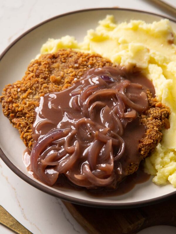 sausage schnitzel on white plate with onion gravy and mash
