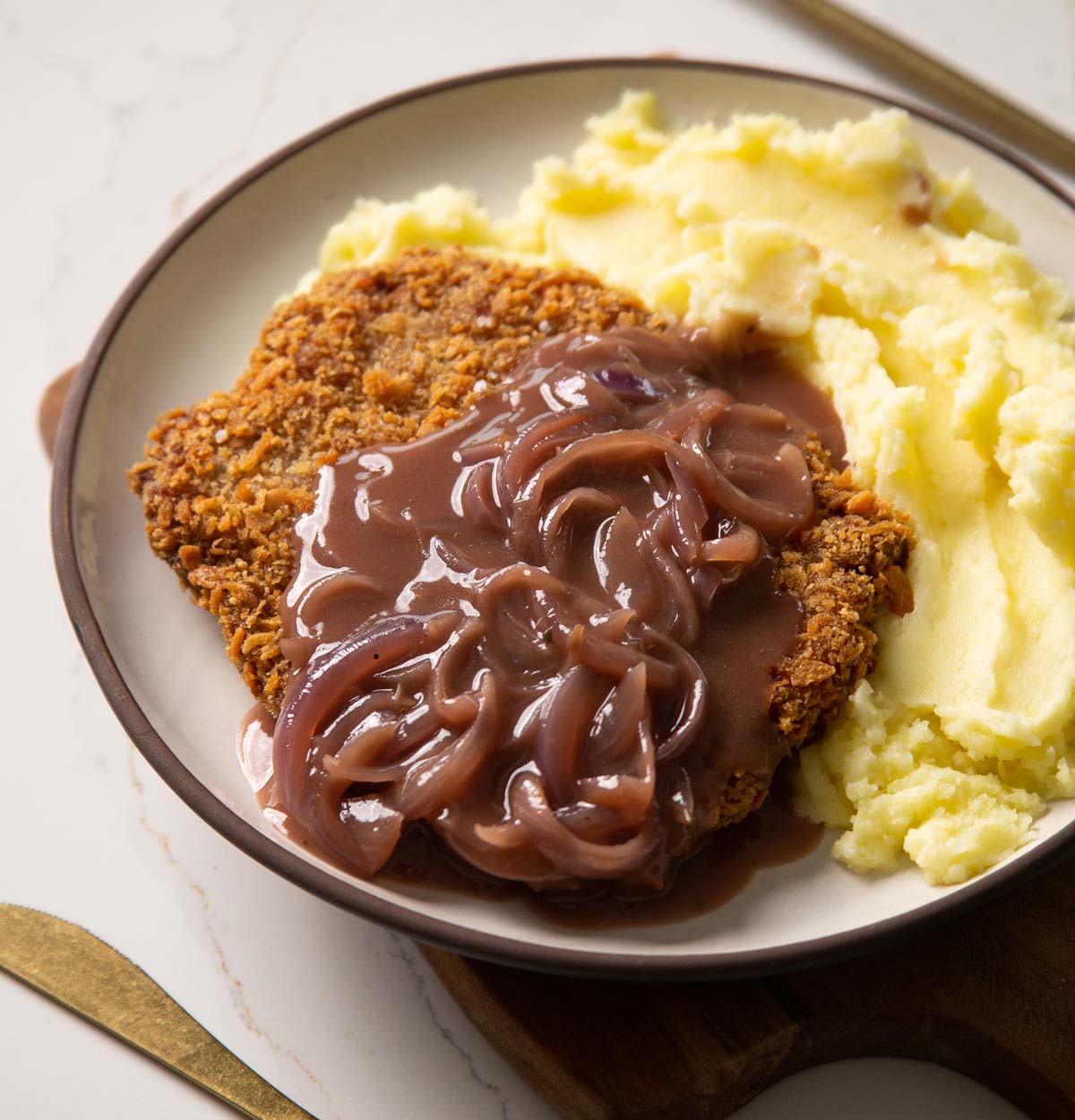 sausage schnitzel with onion gravy and mash on small white plate