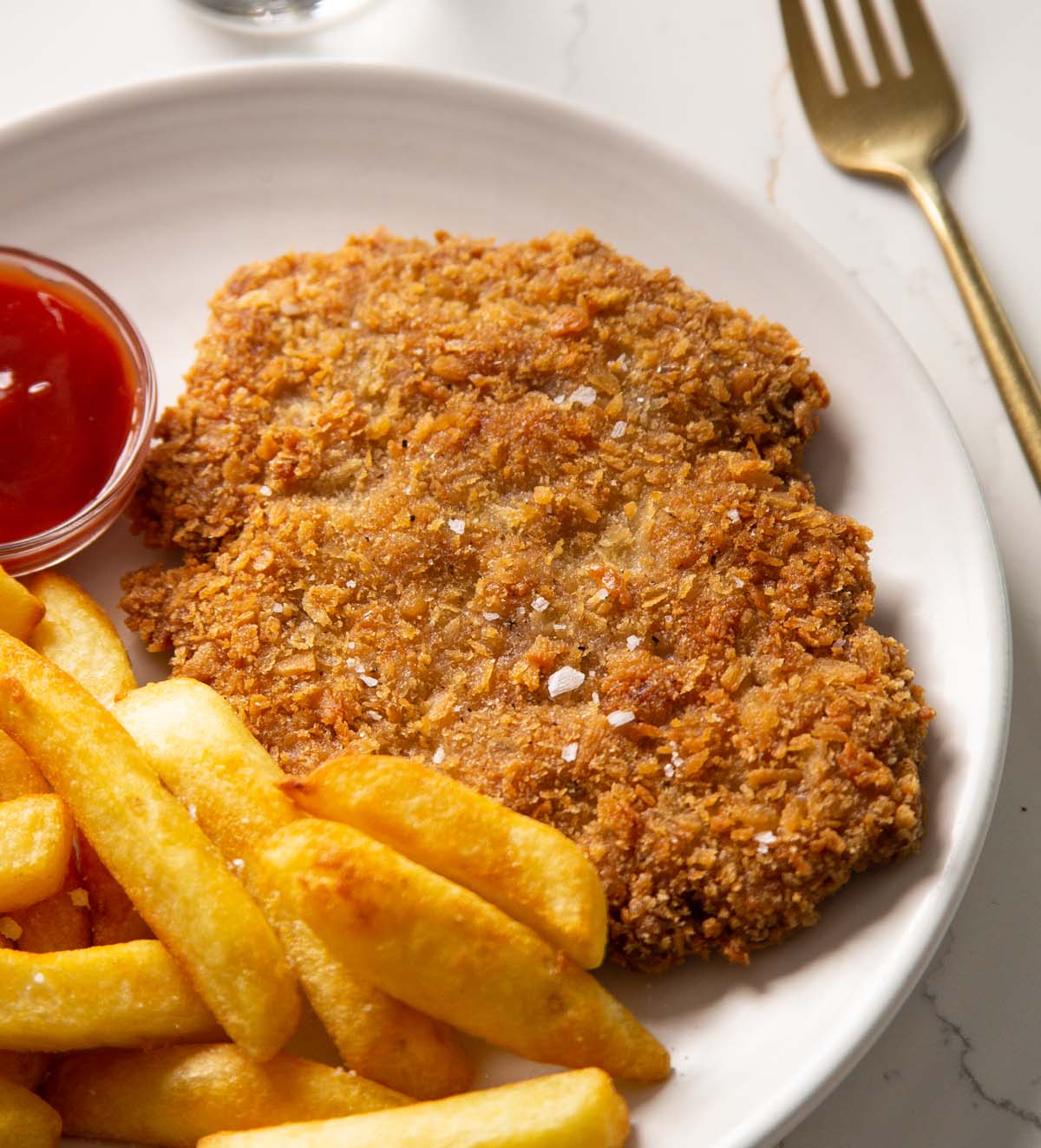 close up shot of sausage schnitzel with chips and ketchup on white plate