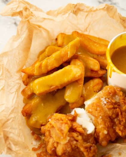 fish and chips covered in curry sauce in scrunched up baking paper