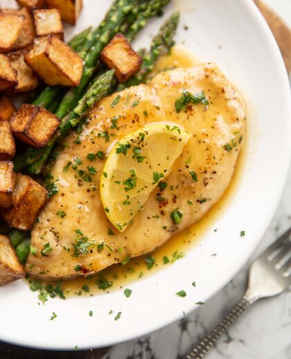 honey lemon chicken breast on small white plate with asparagus and roast potatoes